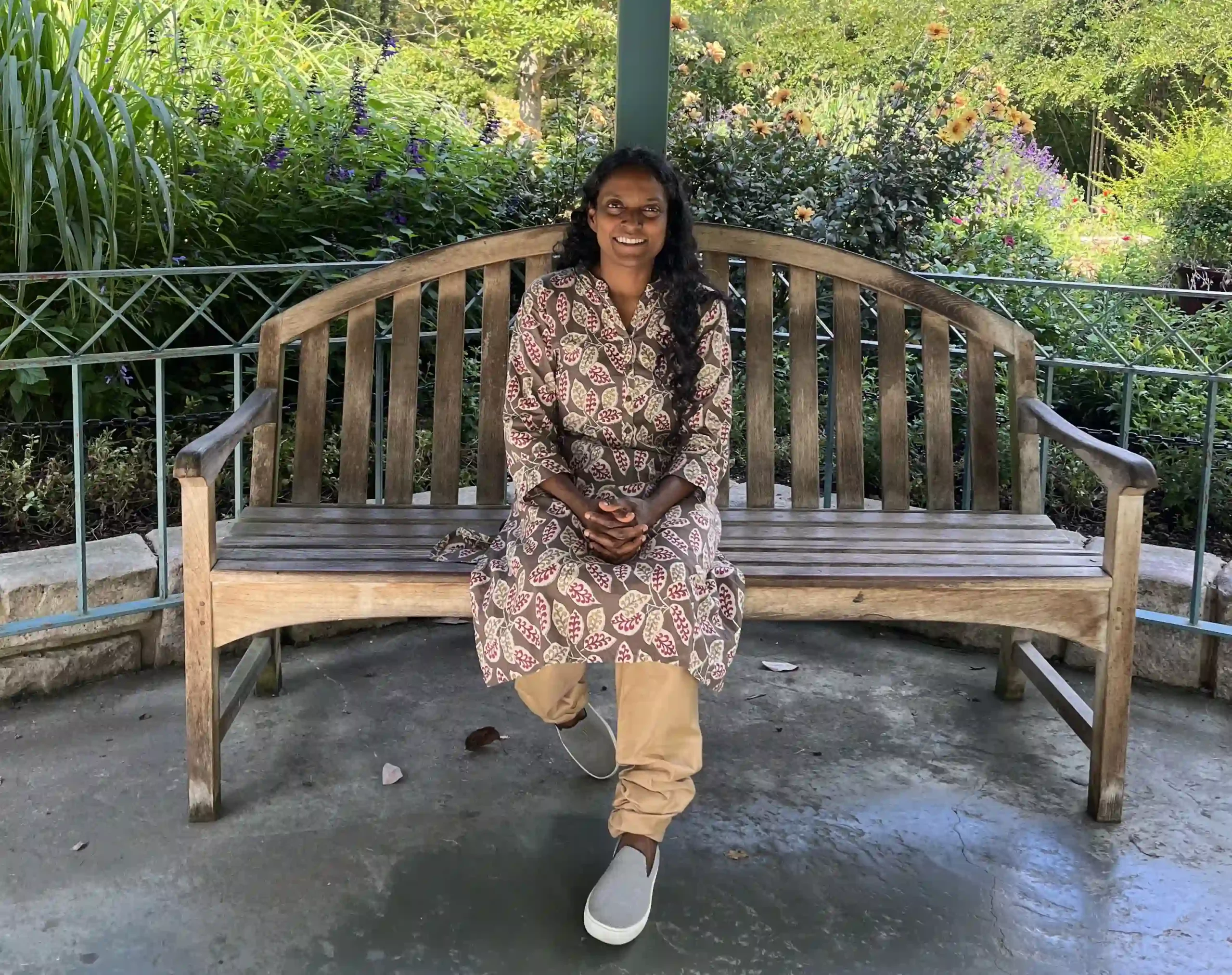 Nurse practitioner Maxine Charles sitting on a bench in a gazebo on a sunny day, wearing a leaf-print dress and khaki pants, smiling, after lowering her A1c on a plant-based diet and reversing prediabetes